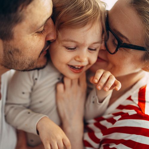 smiling child being kissed by man and woman on the face